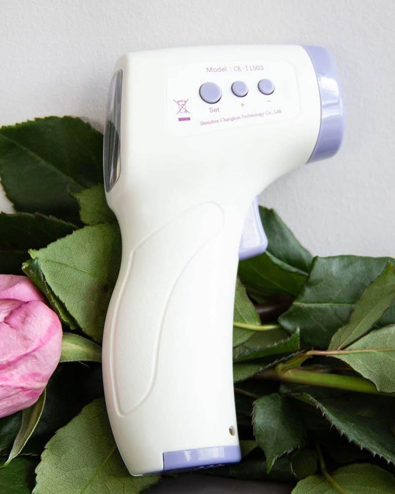 White and purple infrared thermometer on a bed of leaves and roses