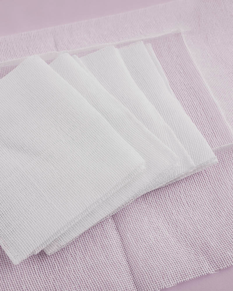 white square cotton gauze pads overlapping each other on a pink background