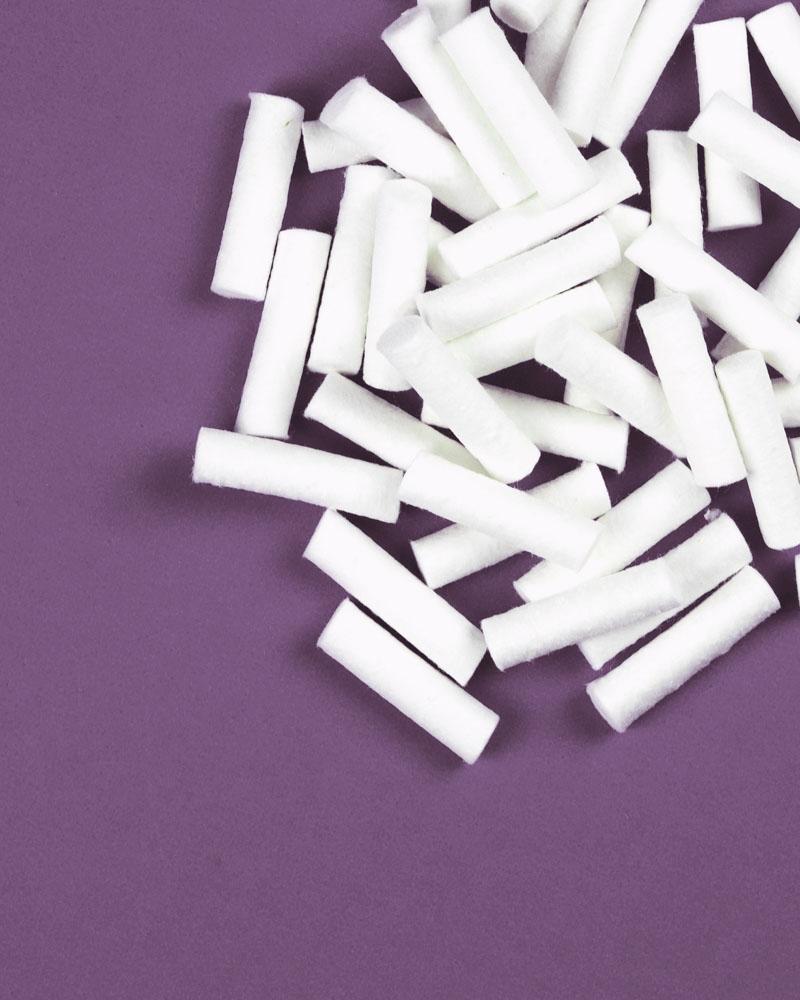 white, short cotton rolls in a pile on a purple background